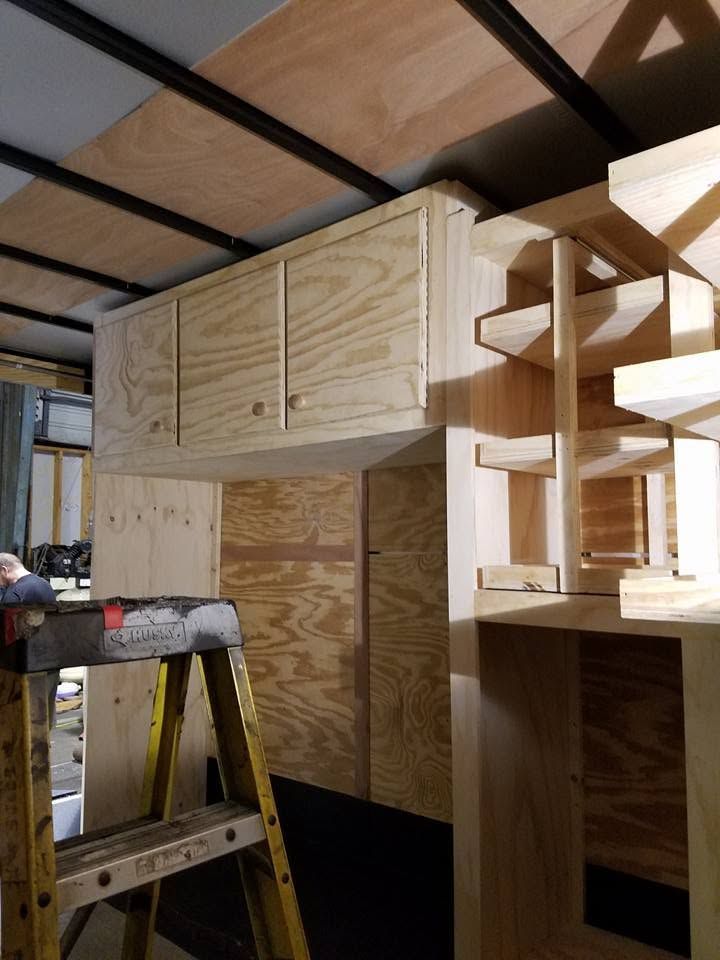 Unfinished plywood loft structure with cabinets and shelves in a workshop, with a ladder in front