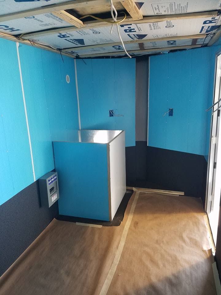 Blue-walled interior room with a small white-and-blue booth and covered floor, under construction.