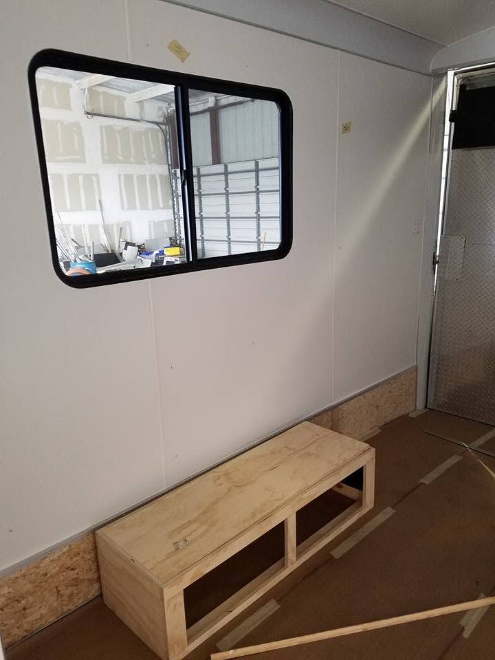 Small room with a white wall, a black-framed window, and a wooden bench or storage unit on the floor.