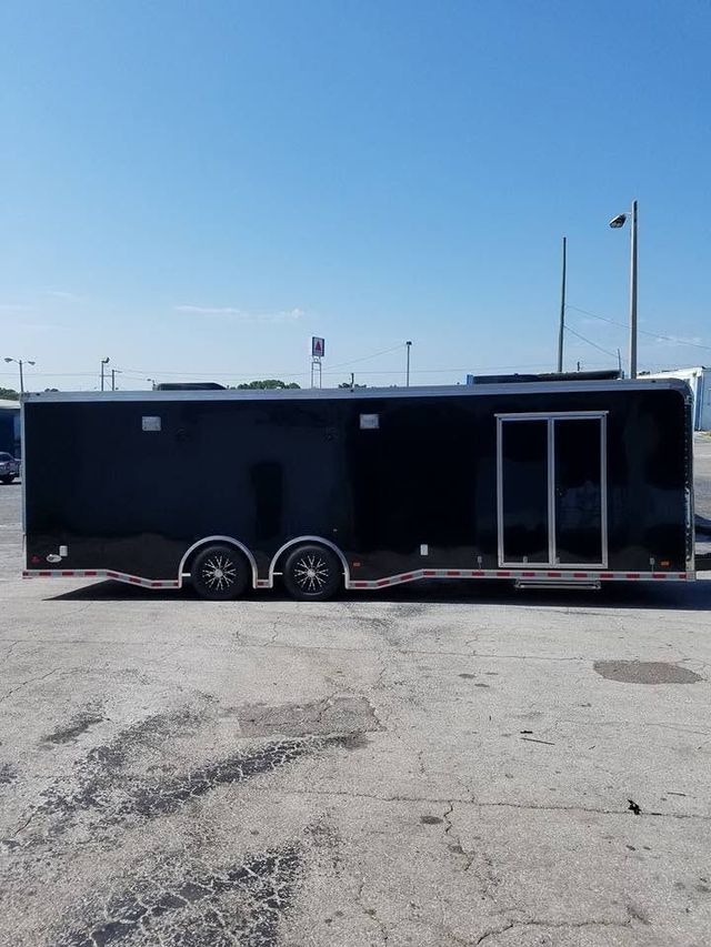 Black enclosed trailer parked on a sunlit gravel lot under a clear blue sky.