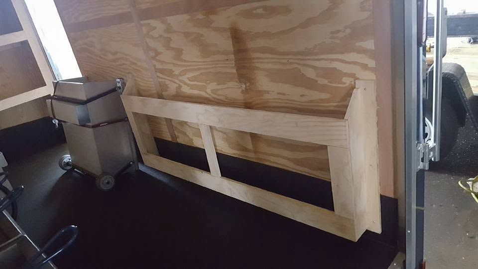 Interior of a van with a plywood-built partition and a small metal cabinet near the rear door.