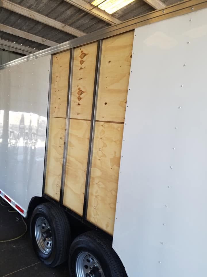 Enclosed cargo trailer with plywood side panel exposed inside a garage or shed.