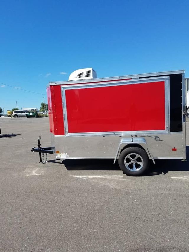 Red enclosed trailer parked on an asphalt lot under a blue sky.
