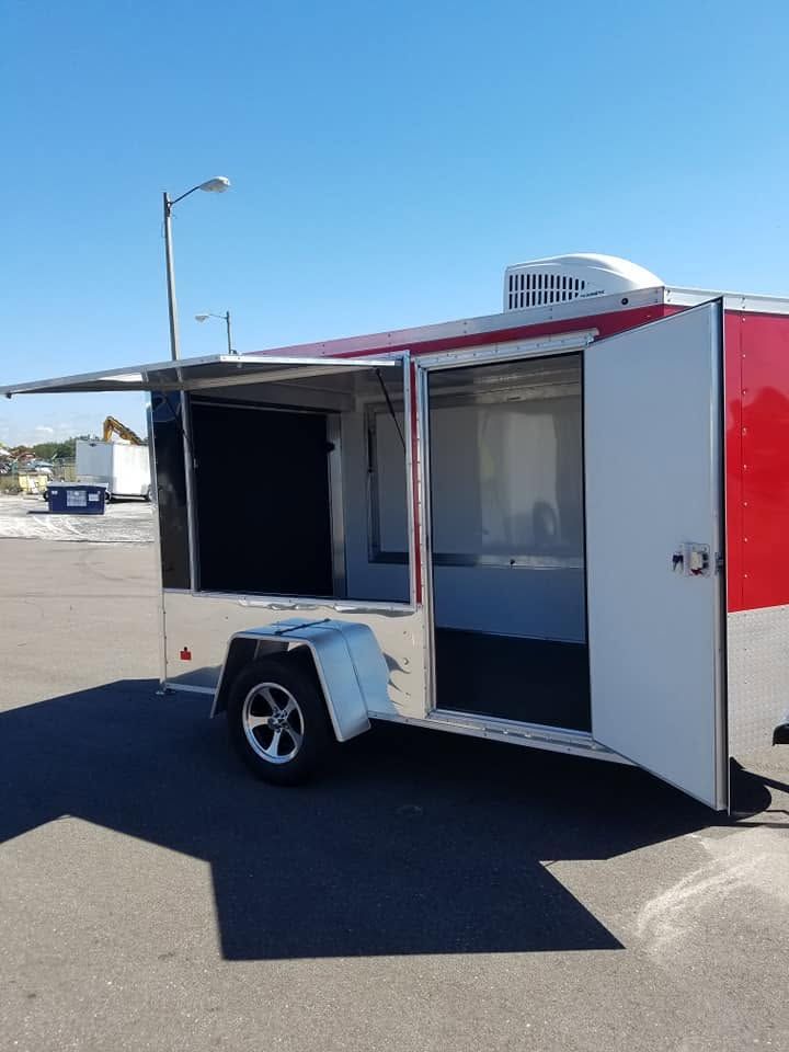 Small white and red enclosed trailer with open side hatch parked in a sunny lot