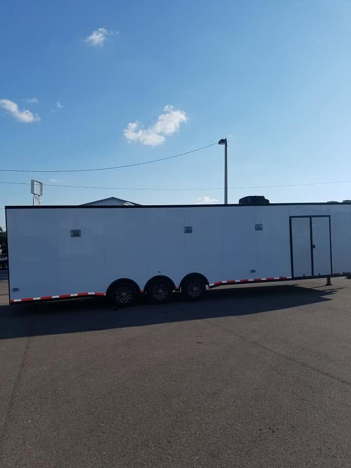 White enclosed trailer parked on asphalt under a clear blue sky