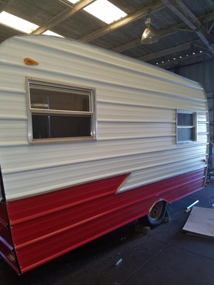 Red and white vintage camper trailer indoors, side view with windows and a wheel visible.