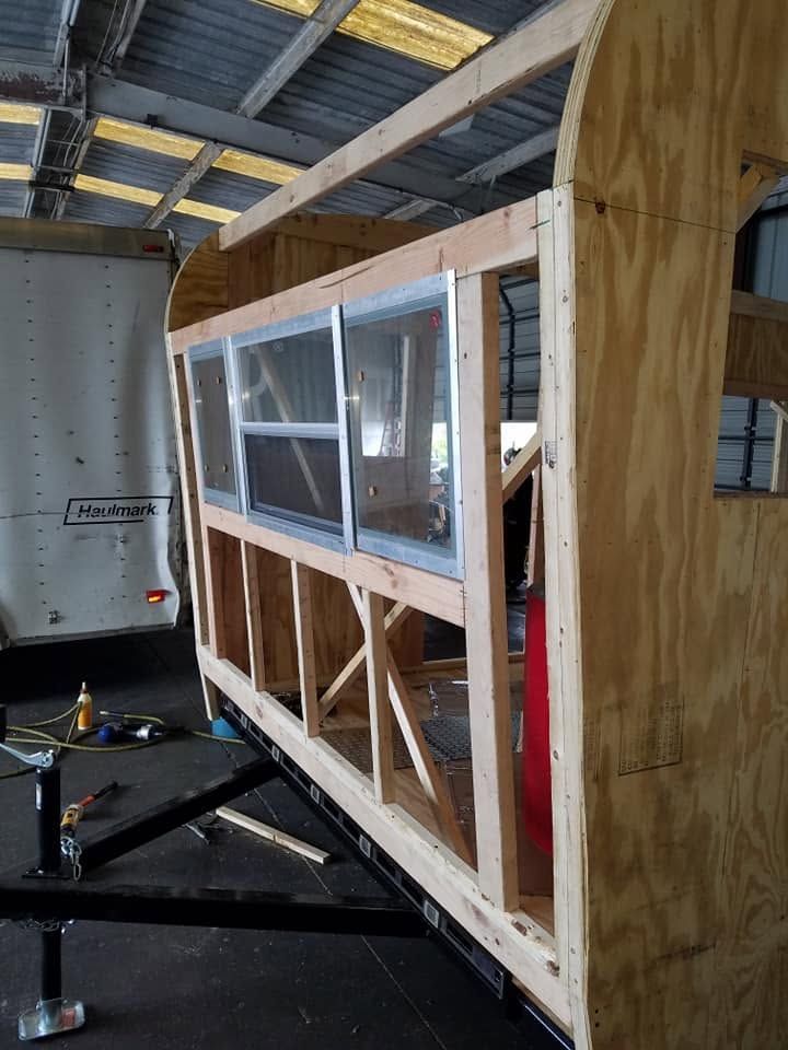 Partially built wooden structure with windows inside a warehouse-like workshop