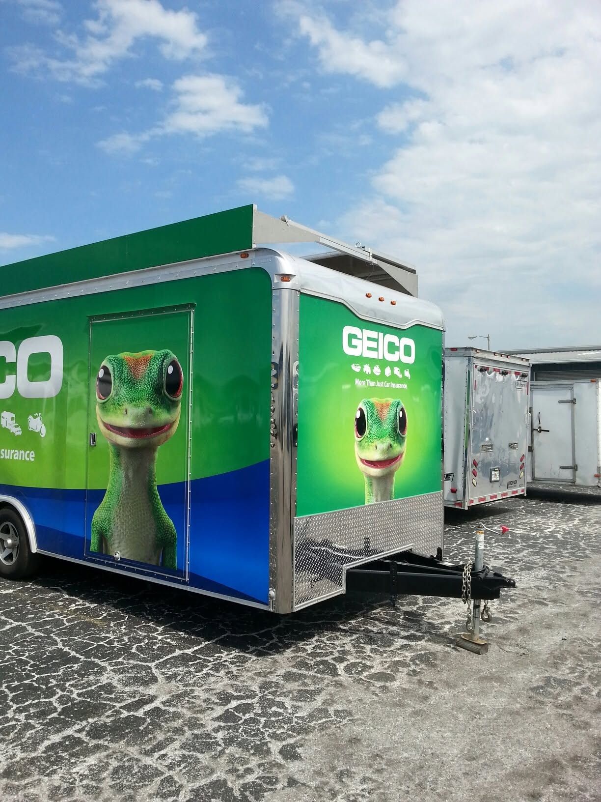 GEICO-branded green box truck on a gravel lot under a blue sky