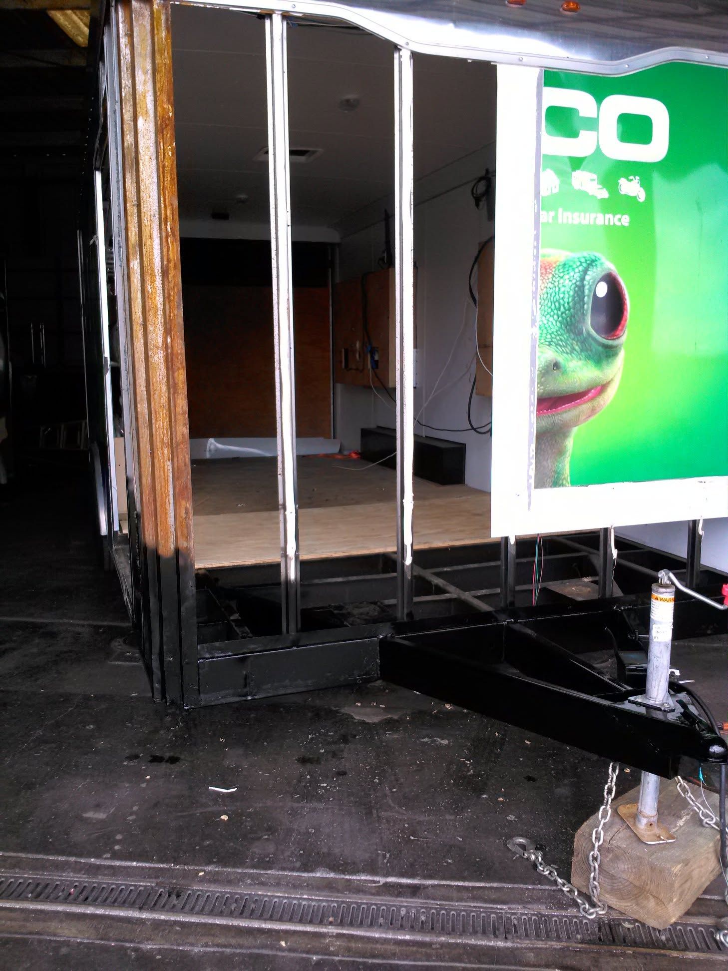 Damaged truck trailer interior with open doors and a green advertisement panel on the side