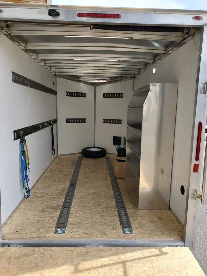 Empty enclosed trailer interior with E-track rails and a spare tire near the front wall