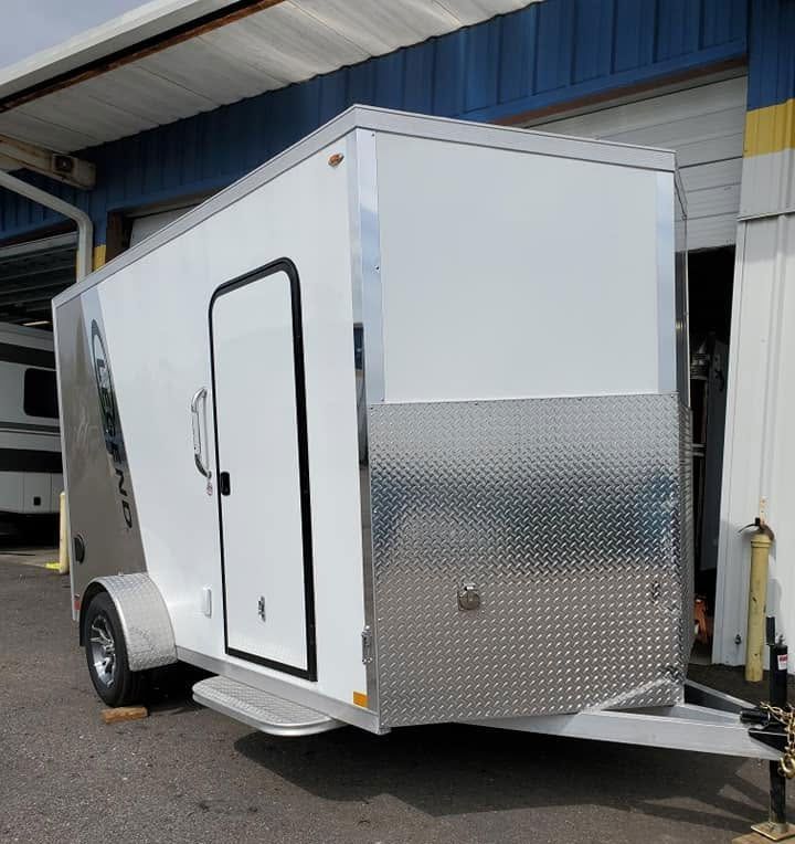 White enclosed cargo trailer with diamond-plate front, parked outside a building.