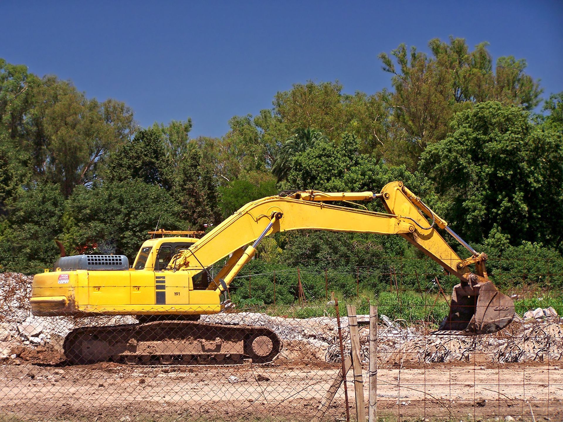 Yellow excavator digging rubble at a construction site with trees in the background