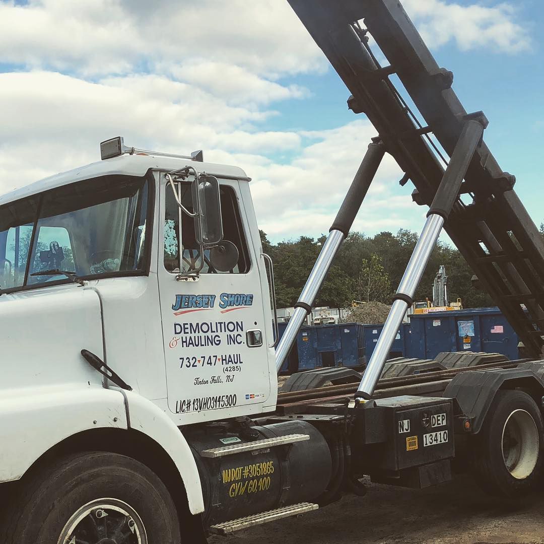 White demolition truck with raised black dump bed at a construction site under a cloudy sky