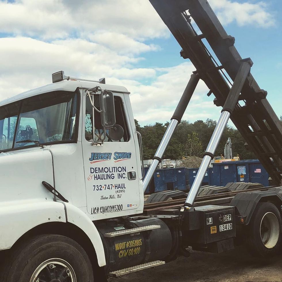 White demolition truck with raised black dump bed at a construction site under a cloudy sky