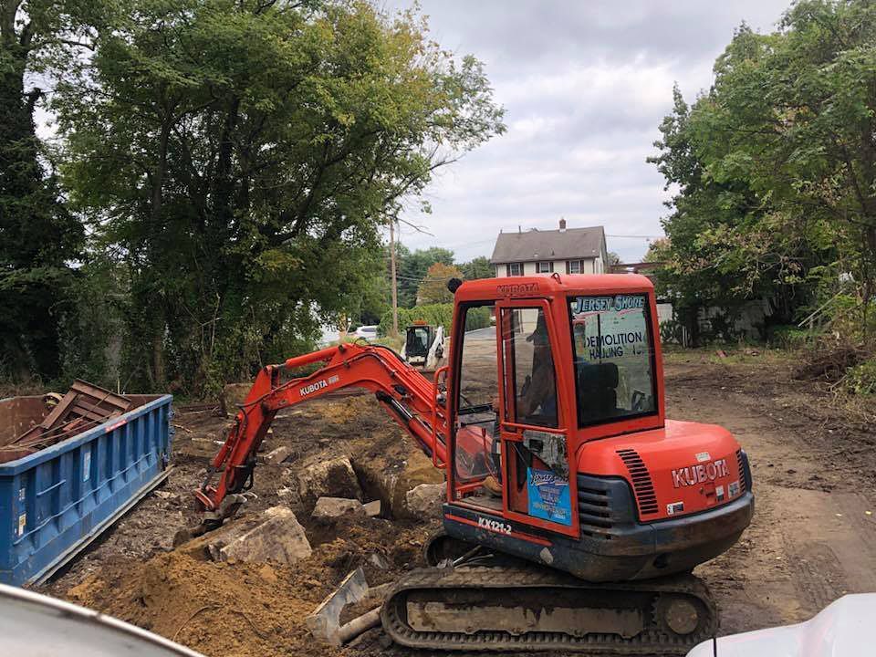 Red excavator moving rocks at a muddy construction site beside a blue dumpster