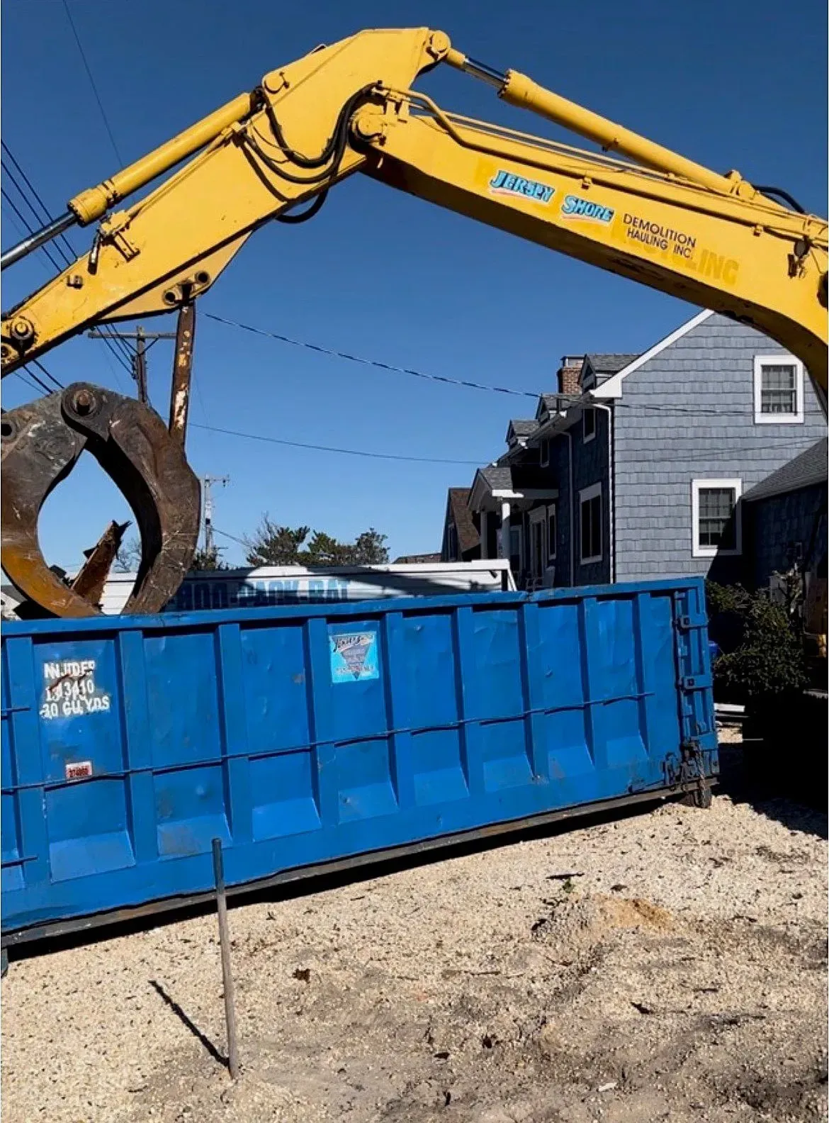 Yellow excavator loading debris into a blue dumpster at a demolition site