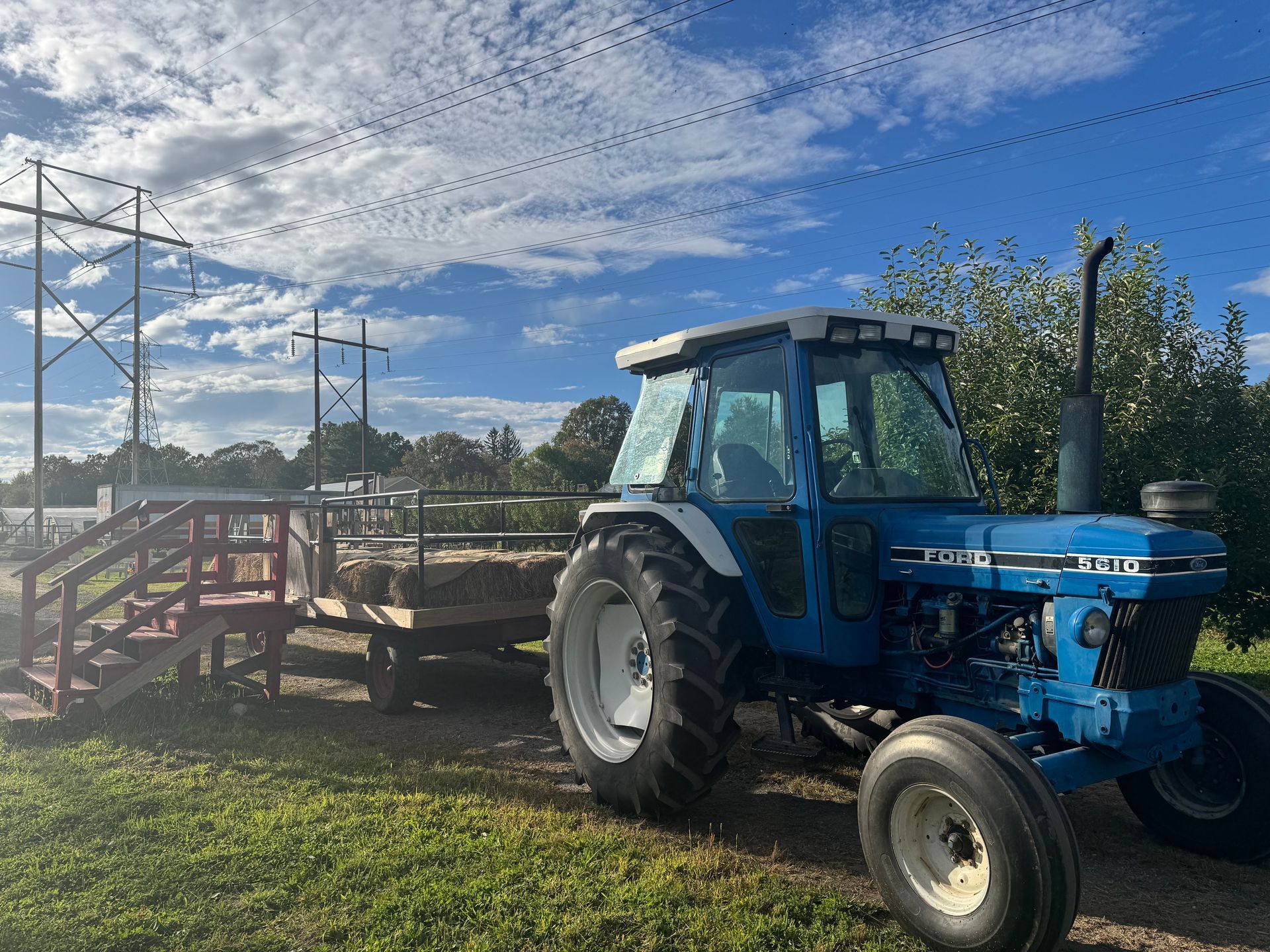 Blue tractor with hay wagon parked on grass under a blue sky.