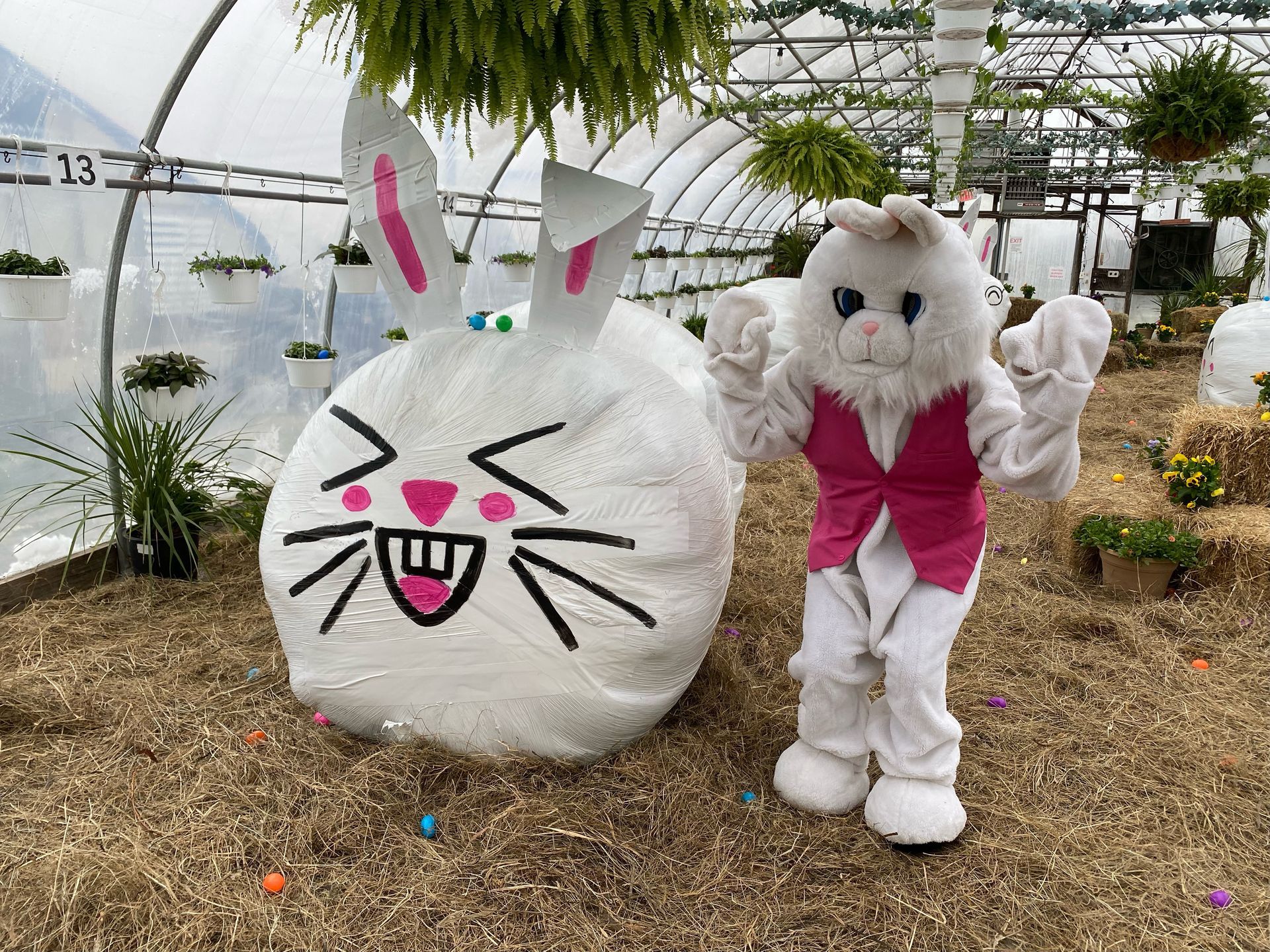 A mascot dressed as an easter bunny is standing next to a large easter egg.