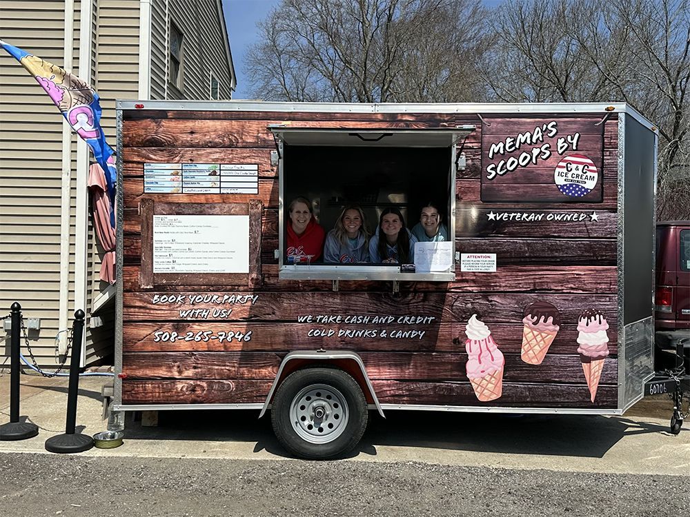 Food truck with wooden siding serving ice cream through a window, parked outdoors with two customers inside.