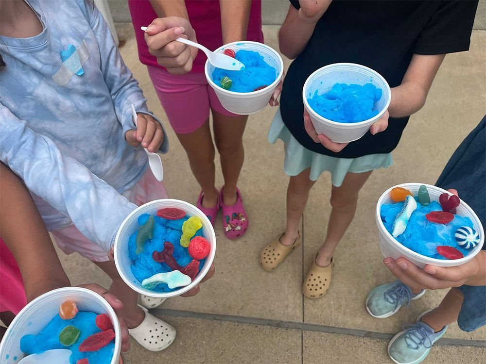Children holding bowls of bright blue shaved ice with colorful fruit toppings outdoors