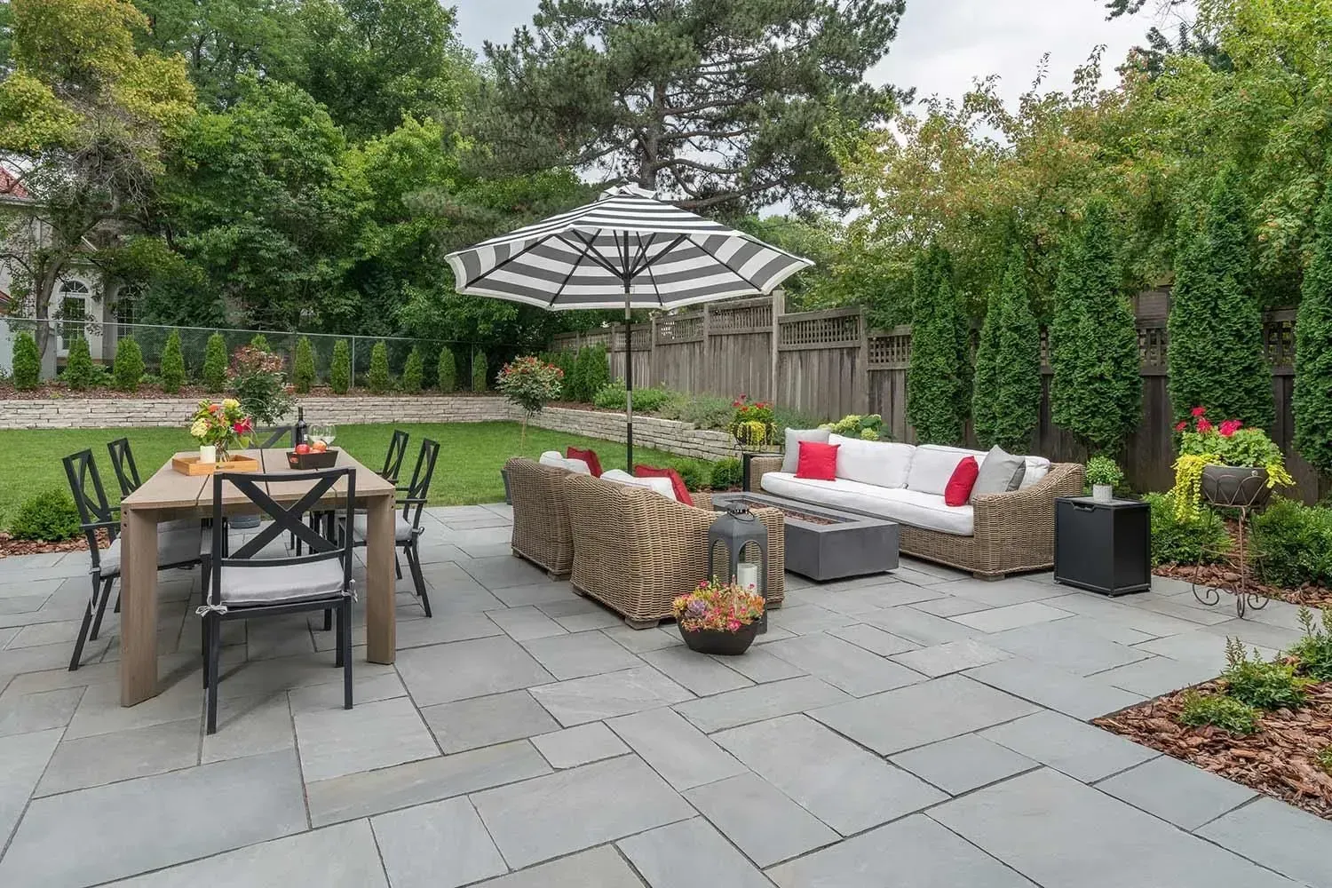 Backyard patio with gray stone tiles, outdoor furniture, and a black and white striped umbrella.