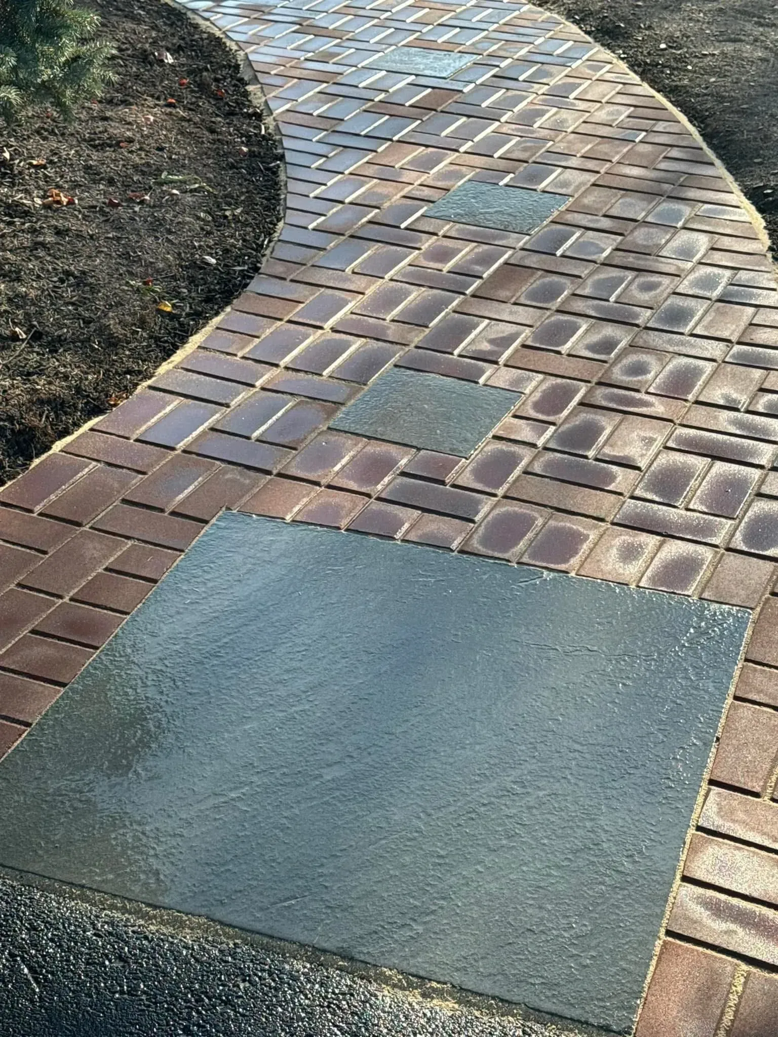 Brick pathway curves through a garden, with three square gray stepping stones integrated into the design.