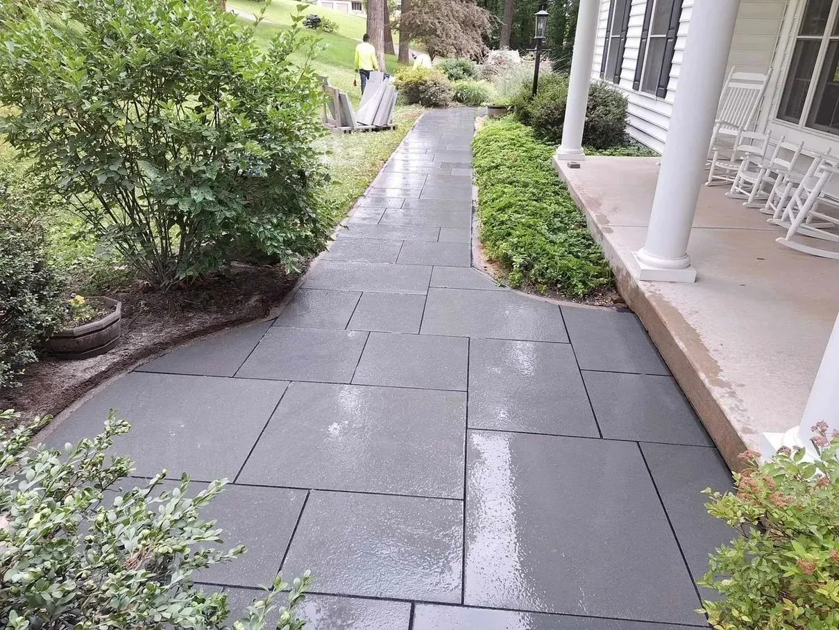 Stone walkway leading to a white porch with columns, flanked by green bushes and plantings.