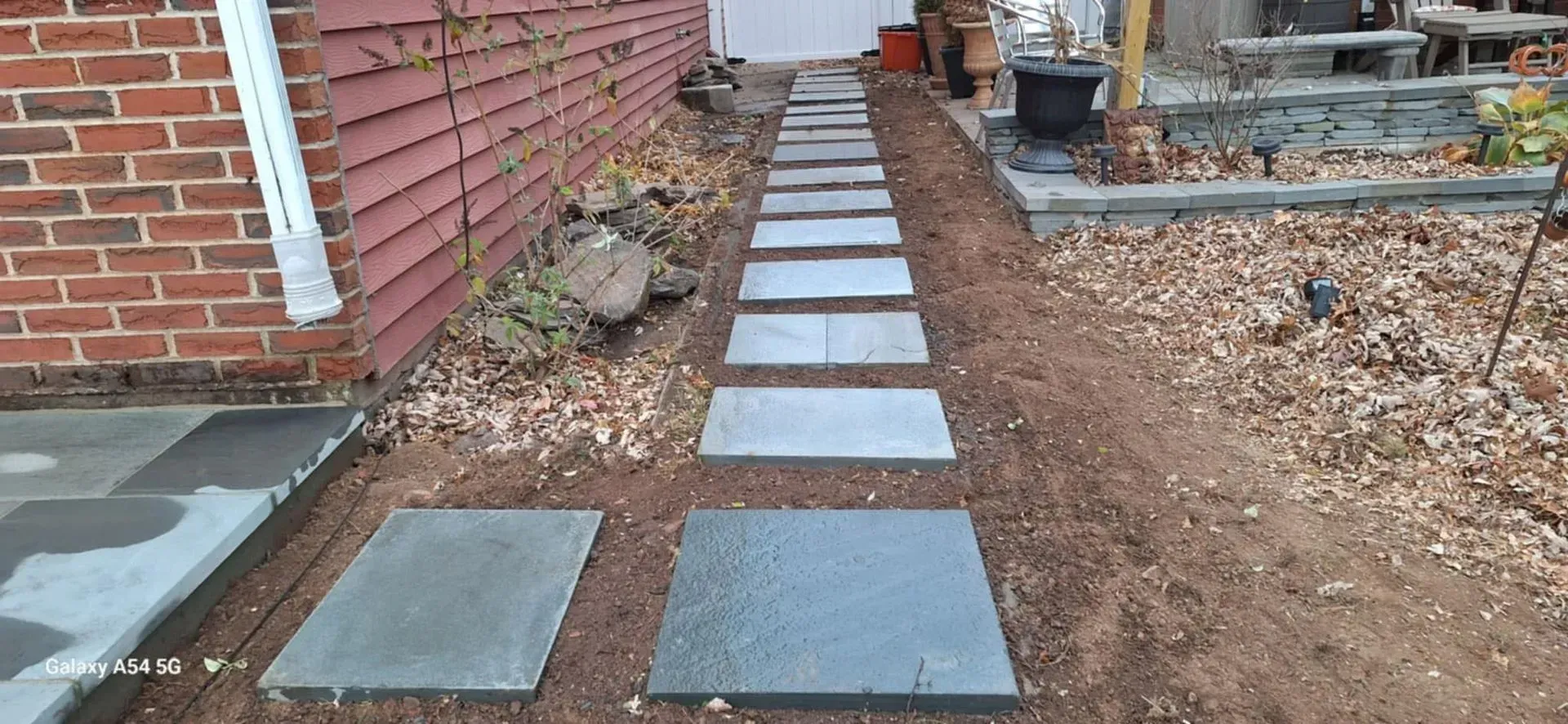 Stone pathway leading towards a white door, flanked by a red brick wall on the left and a gravel garden on the right.