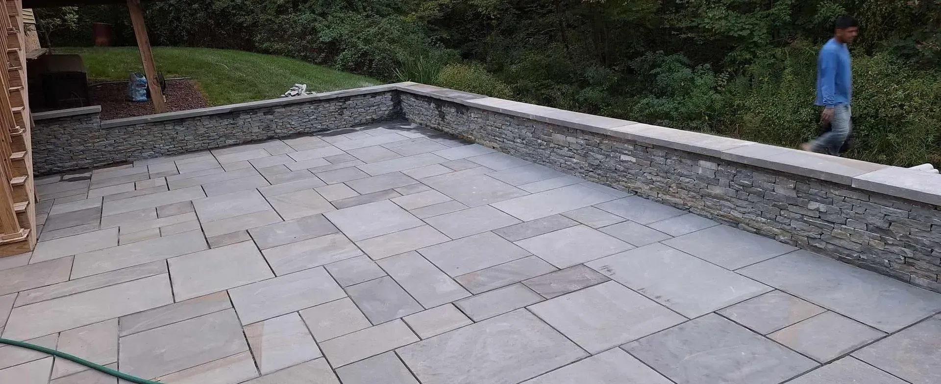 A stone patio with a low stone wall and a person walking in the background.