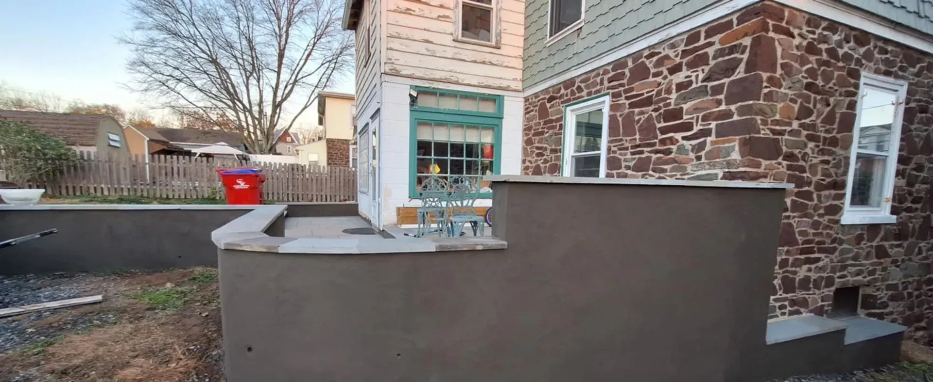 Two people working near a white truck parked in a backyard with stone patio and furniture.