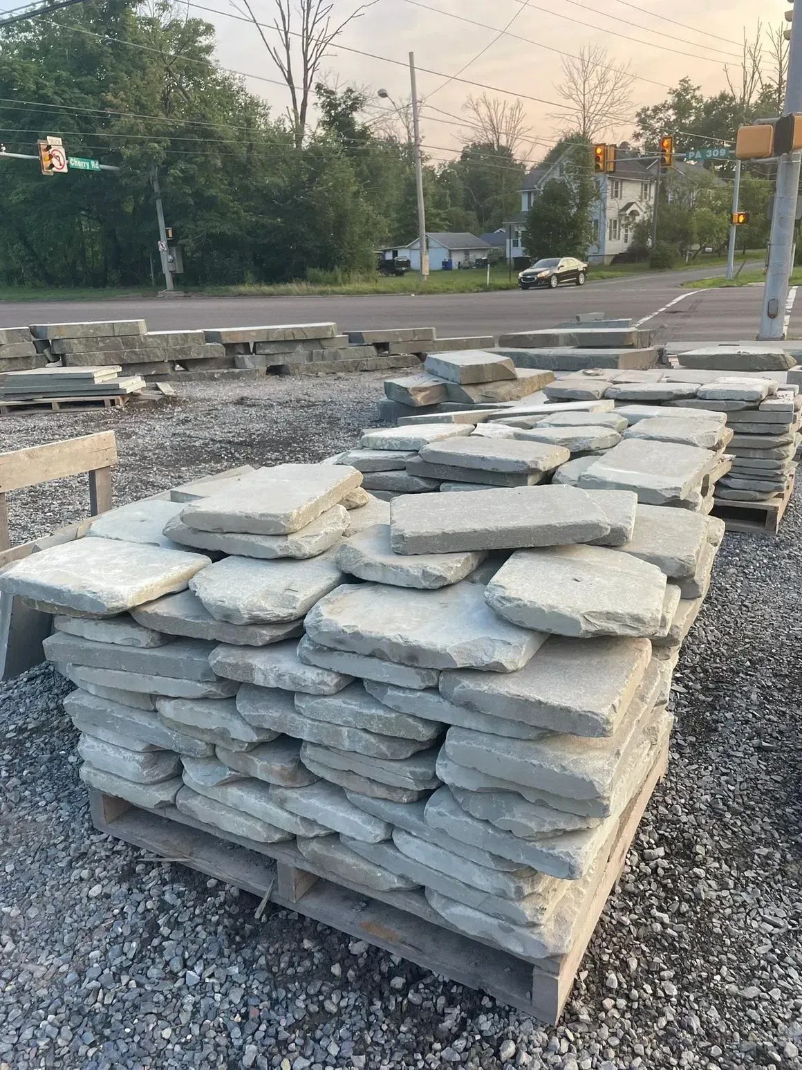 Stacked stone slabs on a wooden pallet outdoors at a business, likely for landscaping. Gray stones are irregularly shaped.