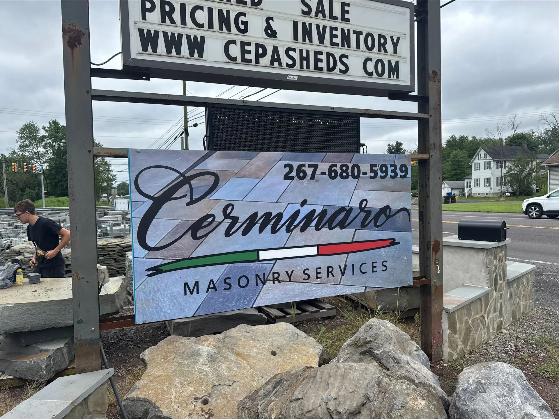 Sign for Cerminaro Masonry Services, featuring the company name and phone number, with a man working nearby.