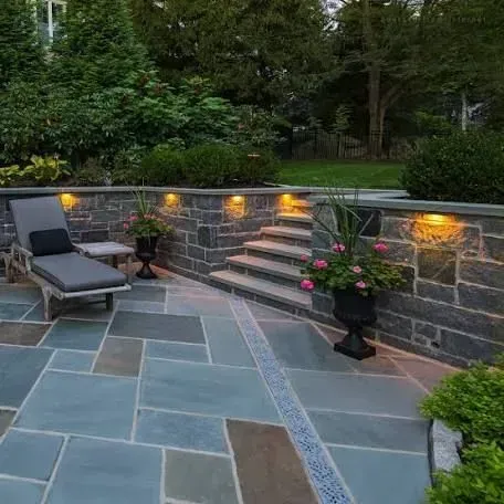 Outdoor patio with stone pavers, seating, retaining wall, and steps. Features include built-in lights and potted flowers.