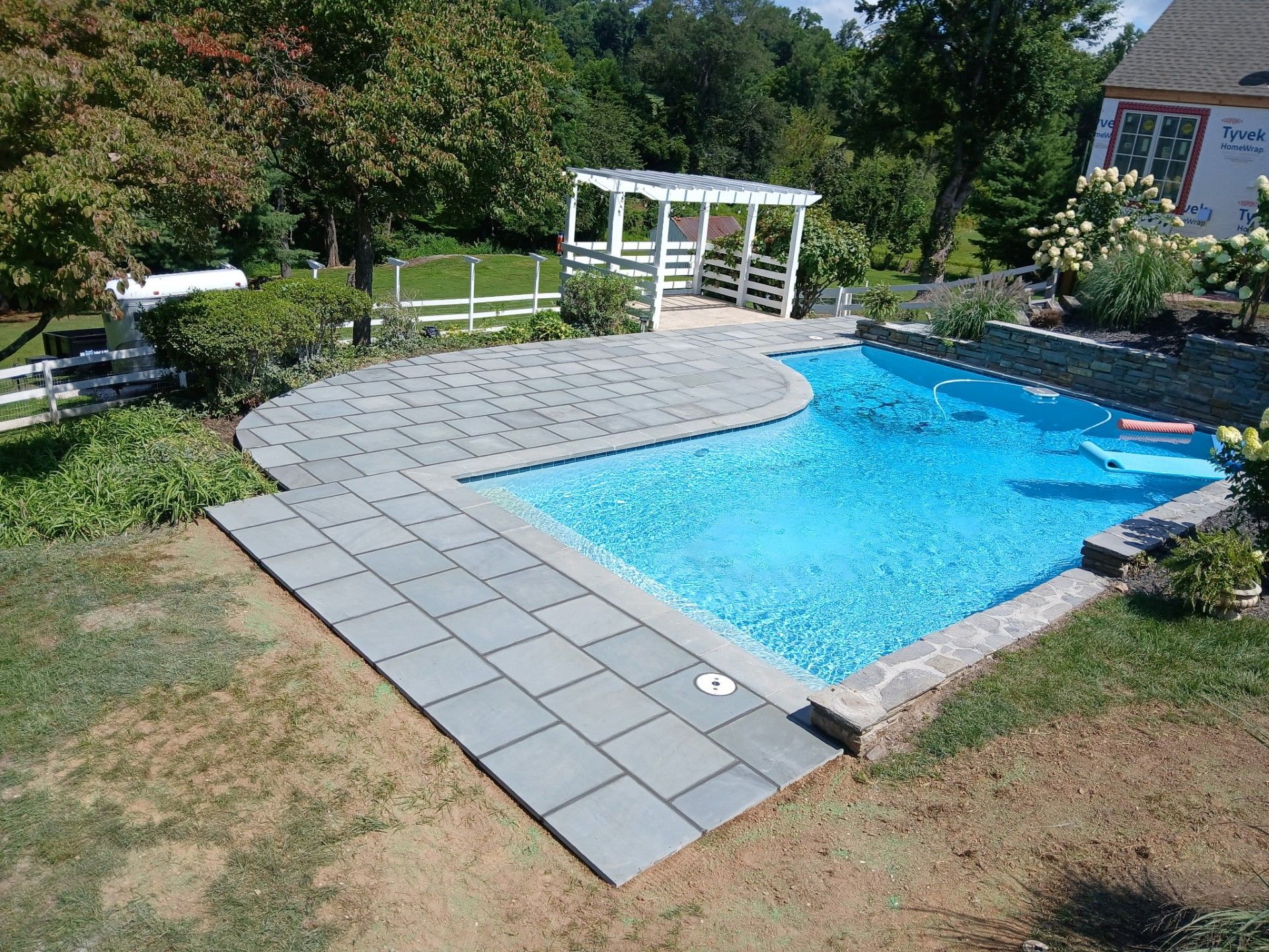 Backyard with a blue swimming pool, gray stone patio, and white pergola.