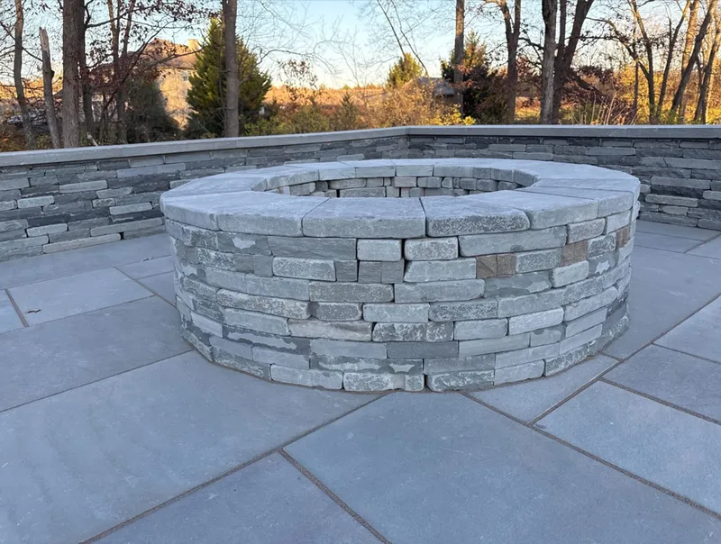 A stone fire pit is sitting on a patio next to a stone wall.