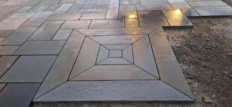 Stone pavers in various shapes and sizes are laid in a pattern with a central square design and surrounding paving.