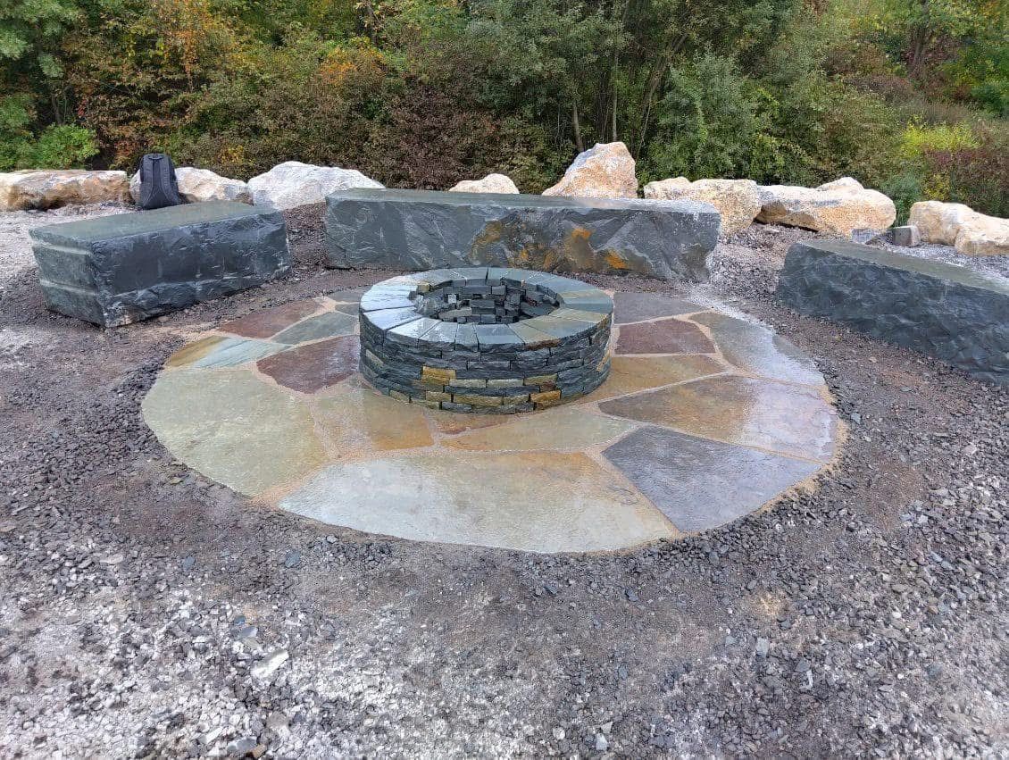 Stone fire pit and seating area in an outdoor setting with natural stone and gravel.