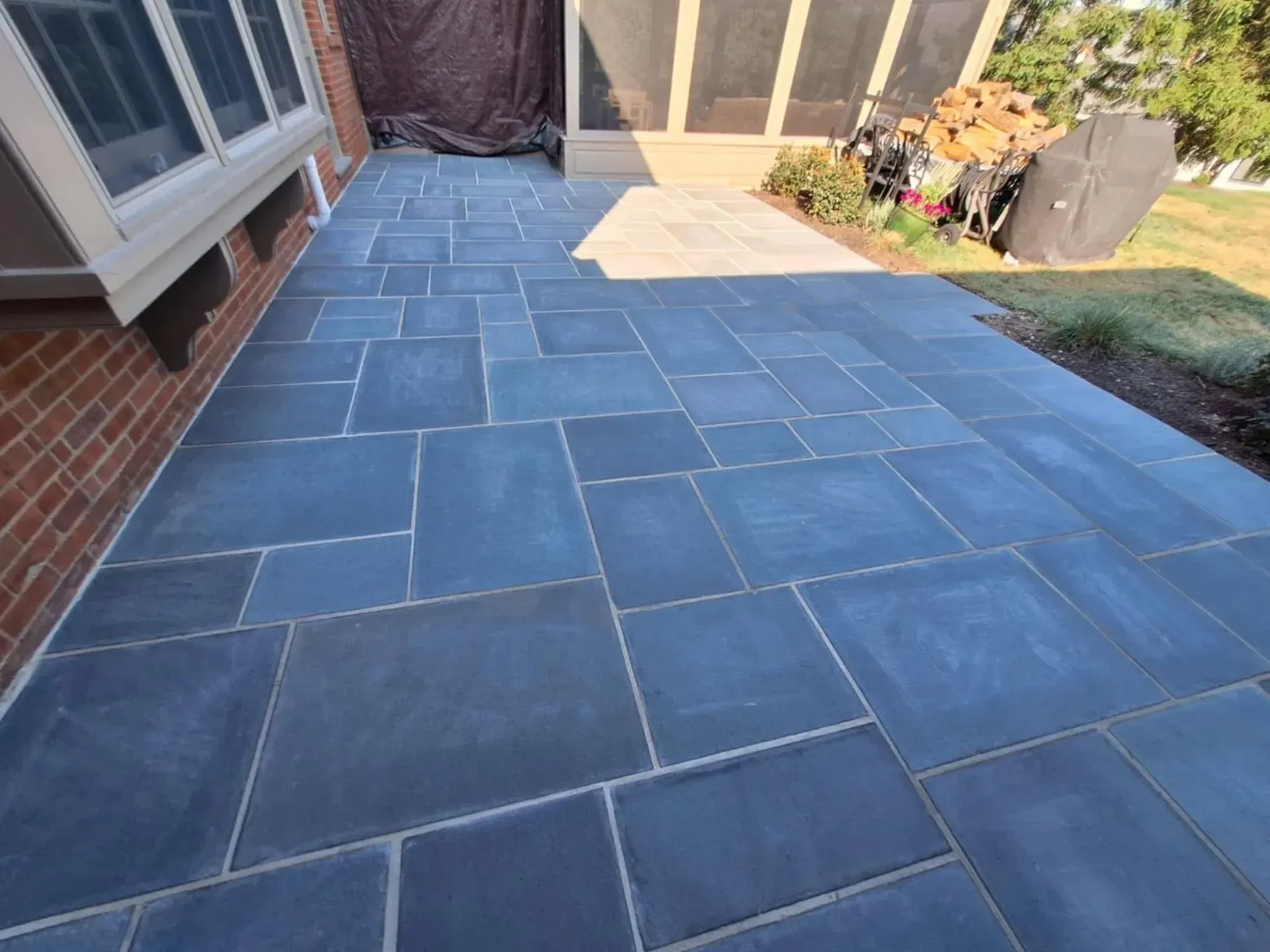 A stone patio with irregular-shaped blue tiles next to a brick building and a screened-in porch.