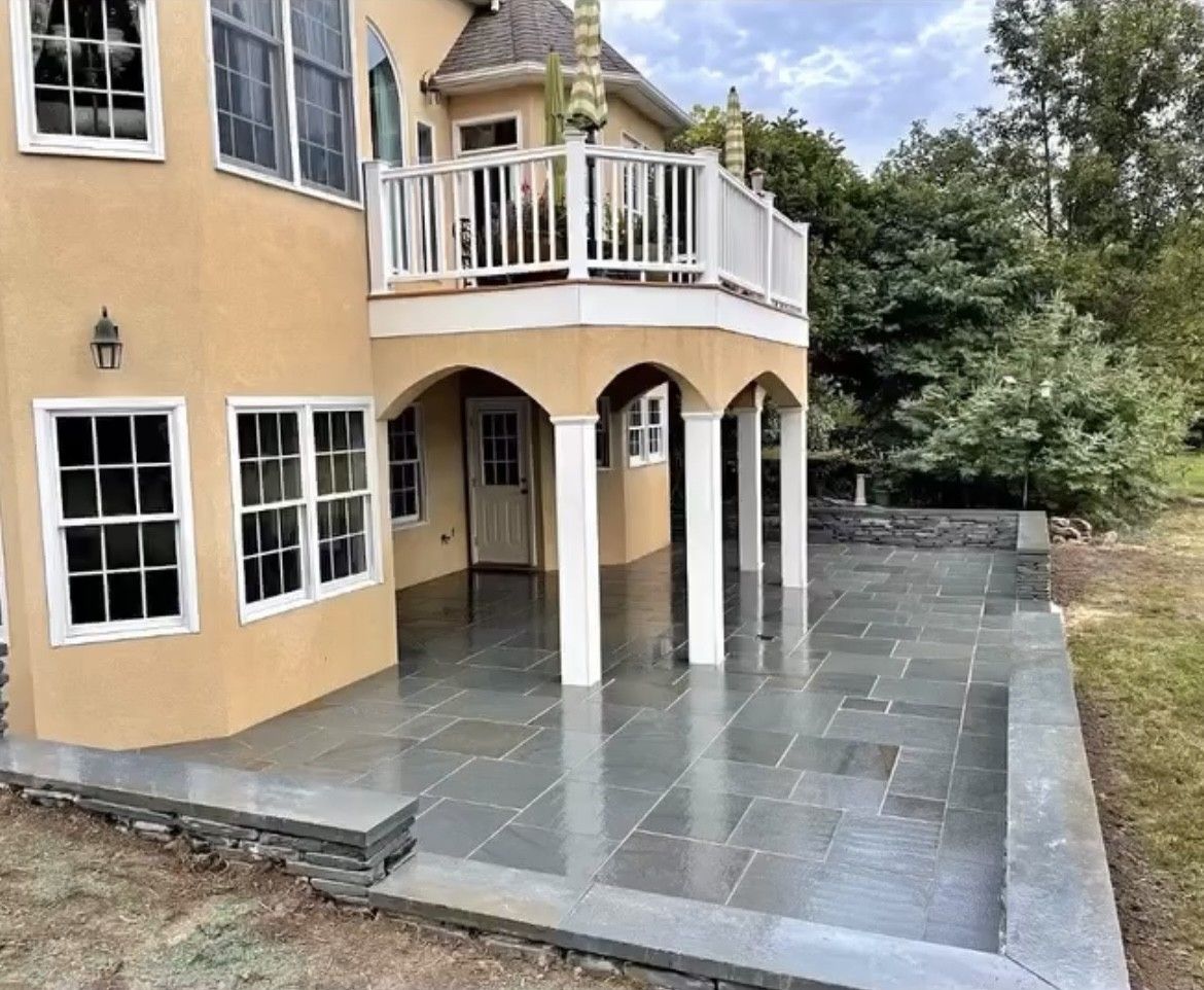 Back patio with stone pavers, supported by white columns, adjacent to a two-story stucco house.