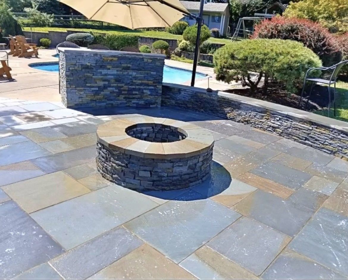 Fire pit and stone patio next to a pool and bar.