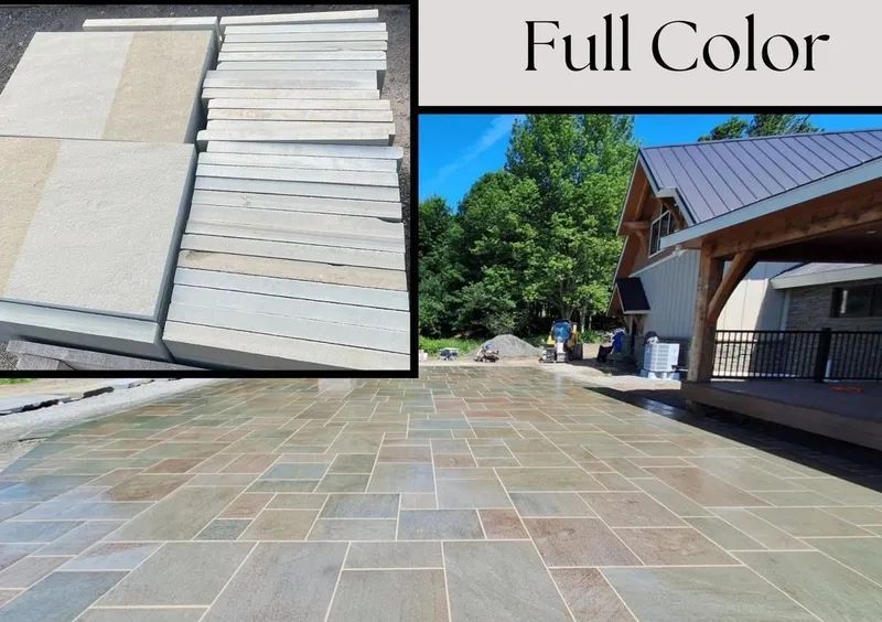 Pile of light-colored stone slabs next to a finished patio of blue-green stone pavers. A house with a porch is in the background.