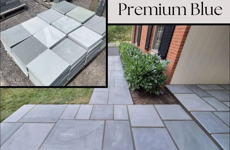 Blue flagstone pavers stacked and laid in a walkway, with a bush, brick building, and grass.