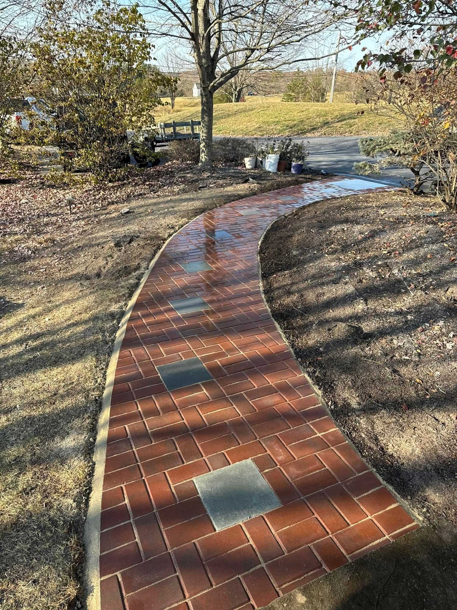 Brick pathway curves through a yard. Red brick laid in a pattern with occasional square, gray tiles.