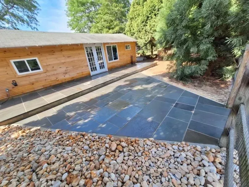 A small wooden building with a stone patio. A gravel bed borders the patio and building.