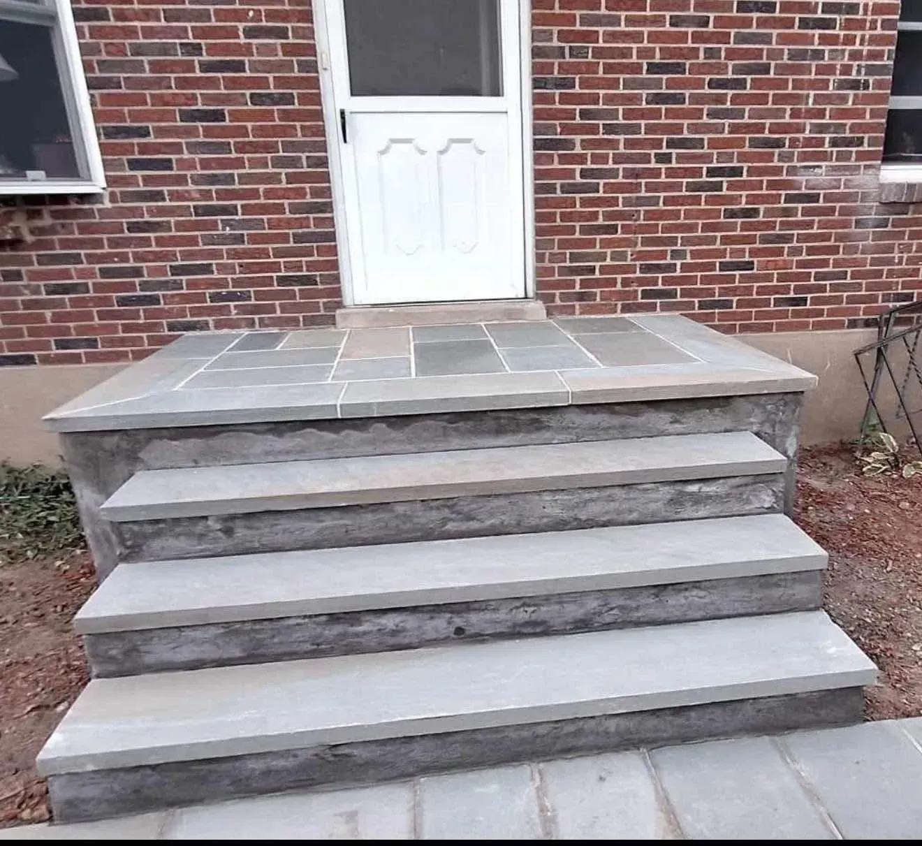Stone steps leading up to a white door on a brick building. The steps and landing are light gray.