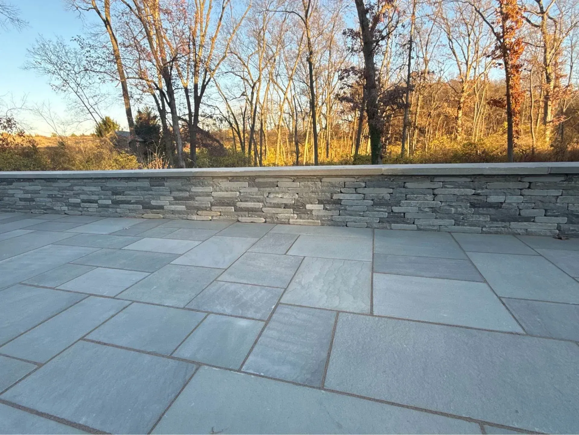 Blue stone patio with a stone wall, surrounded by trees in autumn.