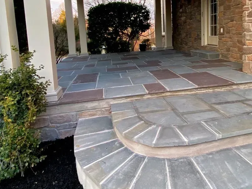 Stone patio with steps leading up to a porch. The patio has rectangular and square blue and red slate tiles.