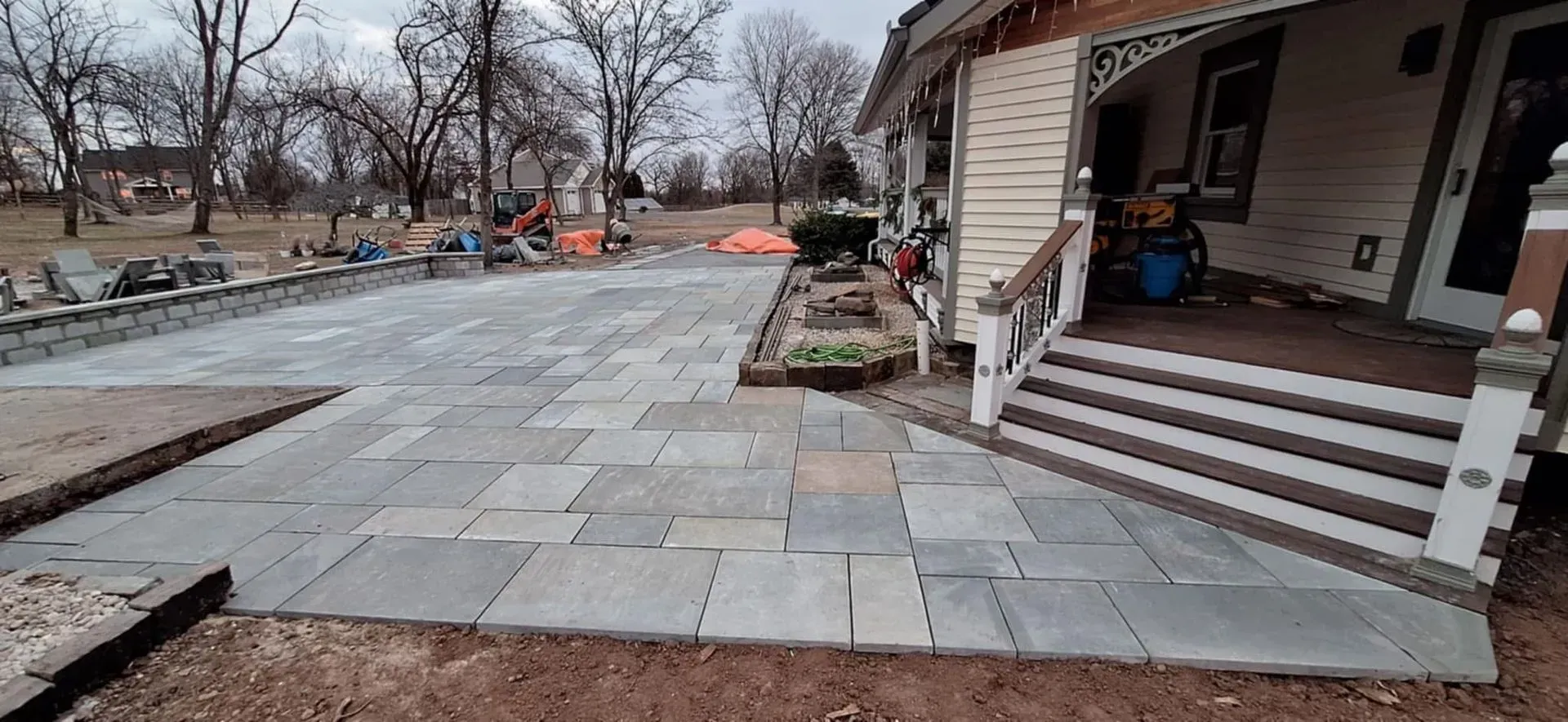 Exterior of a house with a newly constructed patio. Square gray stones make up the patio, leading up to the porch steps.