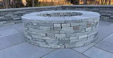A stone fire pit is sitting on a patio next to a stone wall.