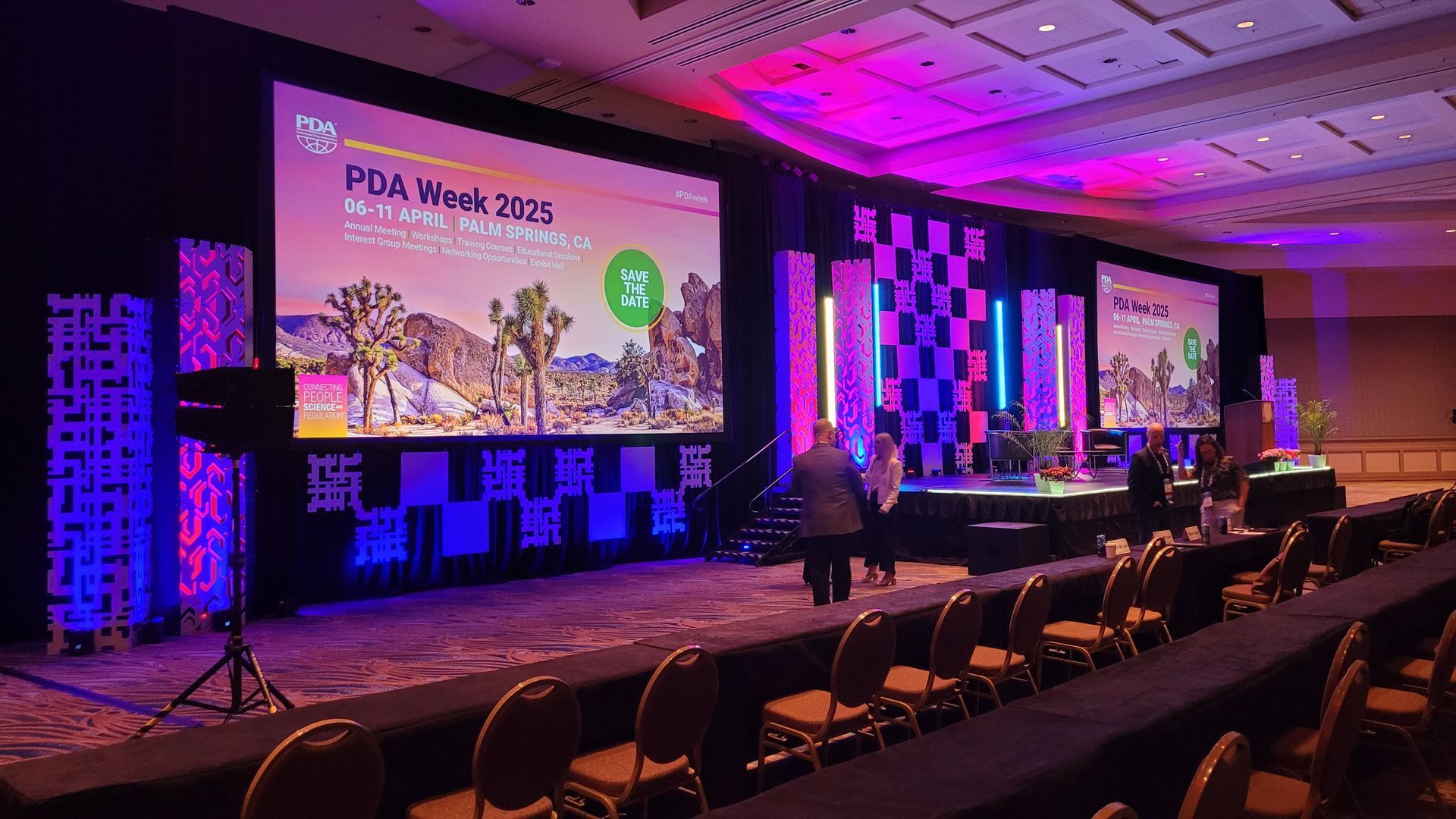 Conference stage setup for PDA Week 2025 with large screens, lighting, and seating; purple, blue, and pink colors.